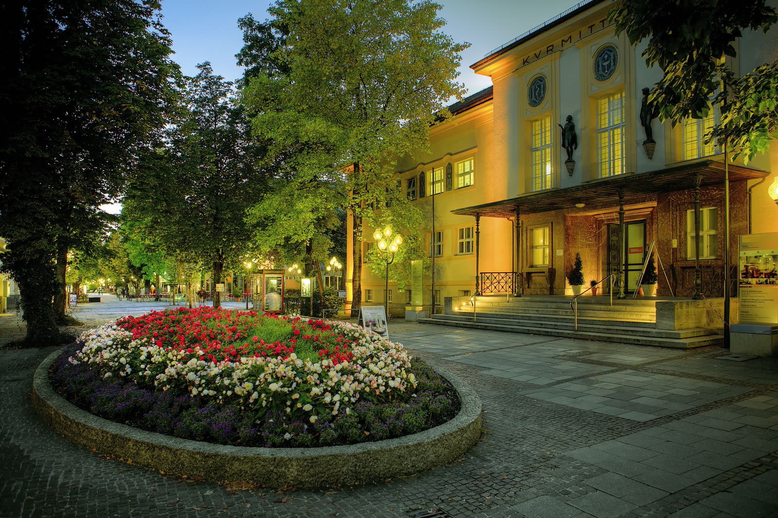Das Kurmittelhaus der Moderne in Bad Reichenhall am Abend, davor die Blumenrabatte der Kurallee